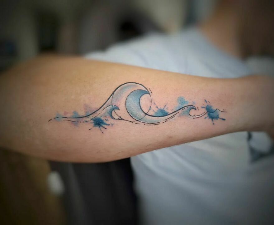 Watercolor tattoo of abstract blue waves on a forearm, showcasing a creative and artistic design.