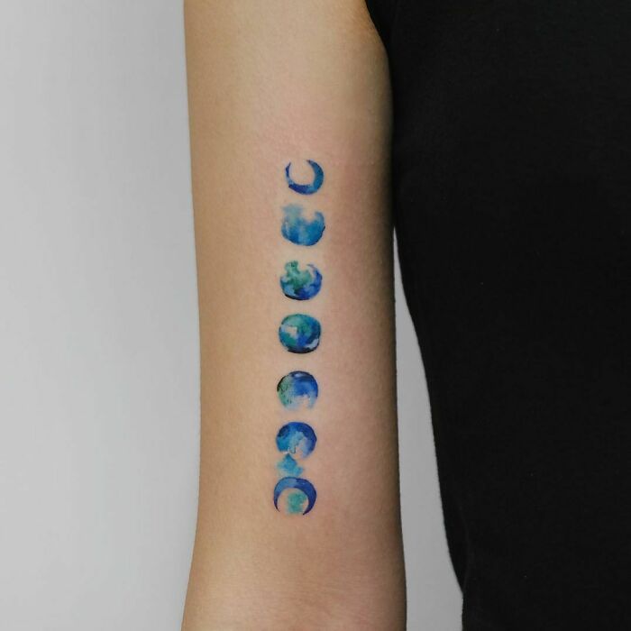Watercolor tattoo of moon phases in vibrant blue and green on an arm, showcasing beautiful inkspiration.