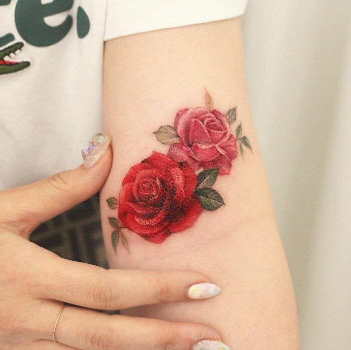 Watercolor tattoo of red and pink roses on forearm, showcasing beautiful inkspiration.