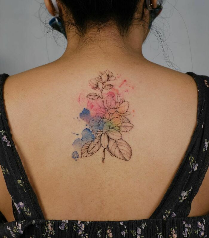 Watercolor tattoo of a floral design on a woman's back, featuring delicate colors and intricate details.