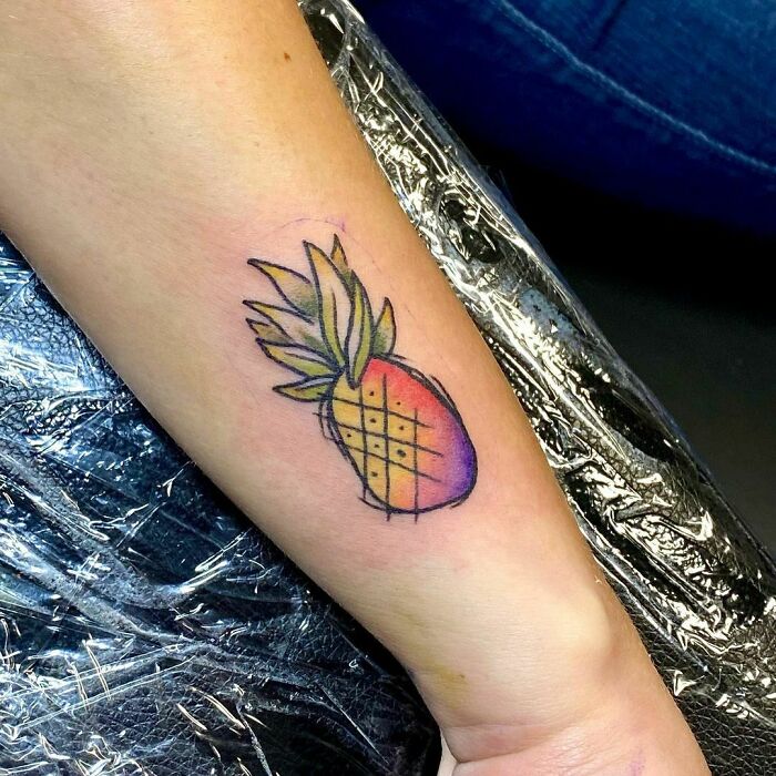 Watercolor tattoo of a pineapple on an arm, blending vibrant colors for inkspiration.