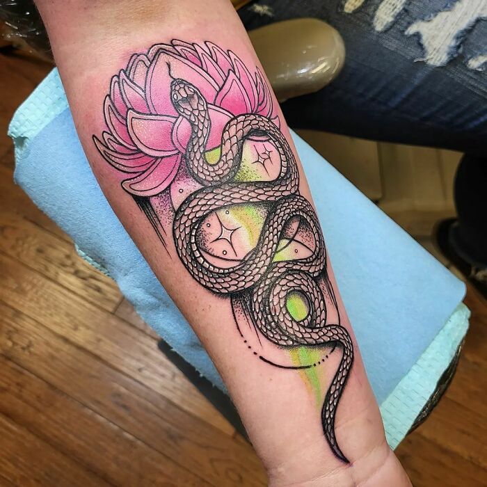 A beautiful watercolor tattoo of a snake with a pink lotus on an arm, providing inkspiration.