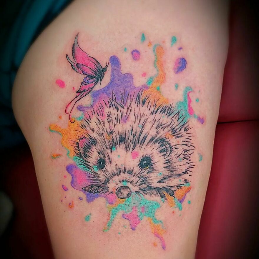 Watercolor tattoo of a hedgehog with colorful splashes and a butterfly, showcasing a creative design idea.