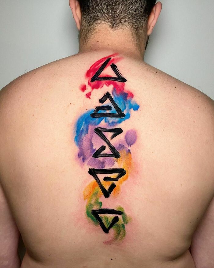 Colorful watercolor tattoo with geometric symbols on back.