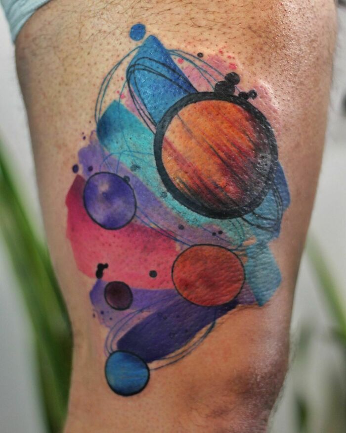 Watercolor tattoo of planets and abstract swirls on a leg, showcasing vibrant ethereal artistry.