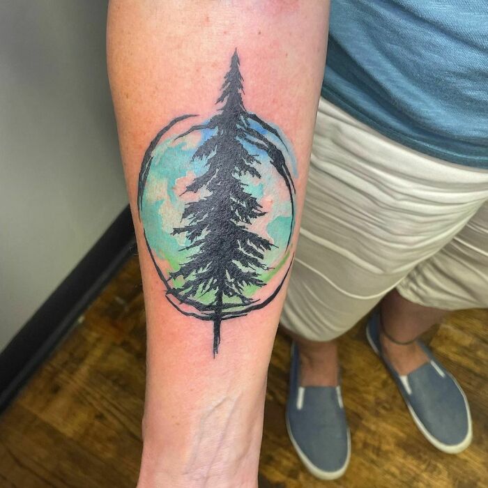 Watercolor tattoo of a tree on a forearm, featuring vibrant blue and green hues for inkspiration.