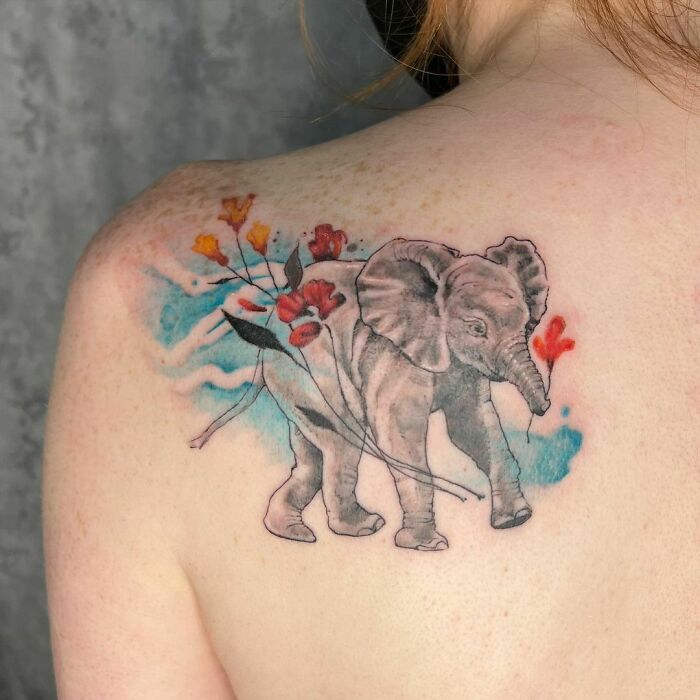 Watercolor tattoo of an elephant with colorful flowers on a person's back, showcasing beautiful inkspiration.