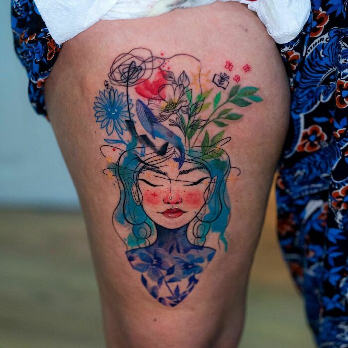 Ethereal watercolor tattoo of a woman with floral elements on her arm.