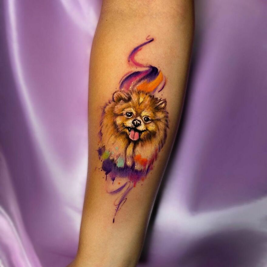 Watercolor tattoo of a dog on forearm, featuring vibrant colors and artistic brushstroke effects.