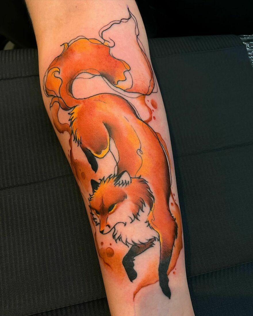 Watercolor tattoo of a vibrant orange fox with flowing ink style on the forearm.