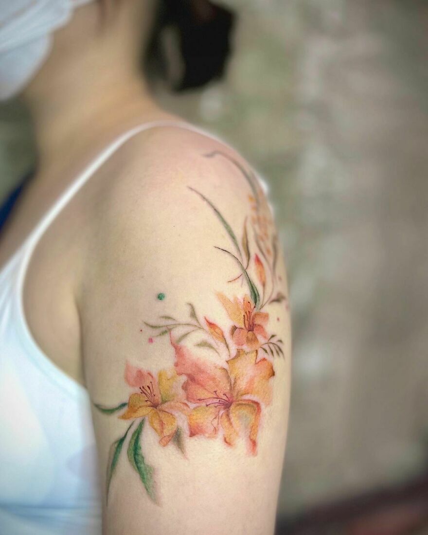 Watercolor tattoo of orange flowers on an arm, showcasing delicate and artistic design elements.