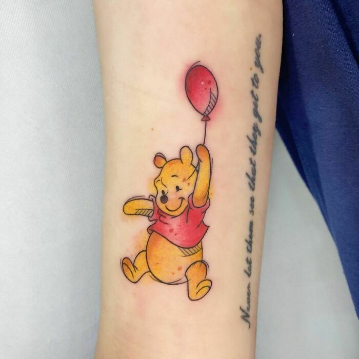 Watercolor tattoo of a cartoon bear with a red balloon on an arm, next to script text.