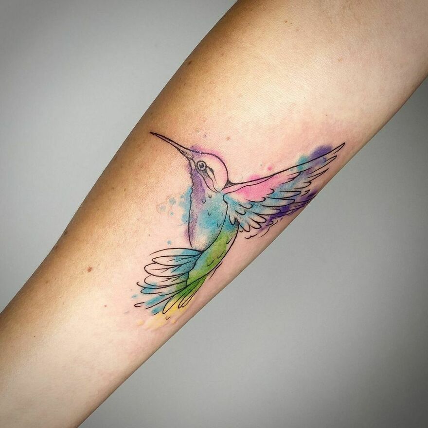Watercolor tattoo of a colorful hummingbird on forearm, showcasing beautiful design.