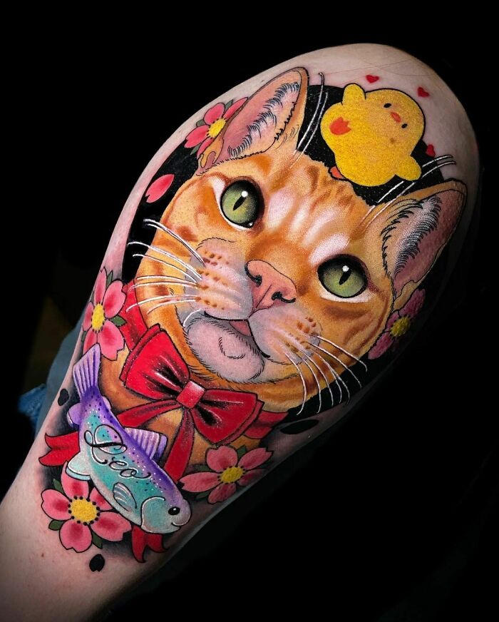 Cat tattoo with flowers and a red bow, featuring colorful fish and yellow cartoon bird, celebrating adorable pets.