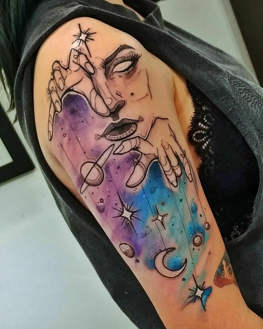 Watercolor tattoo featuring celestial elements and a face, with vibrant colors and cosmic design on an arm.