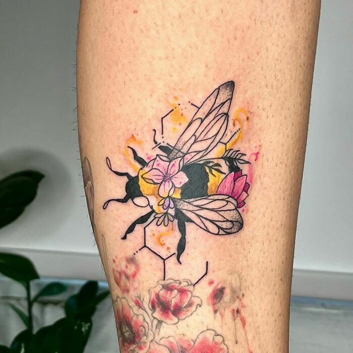 Watercolor tattoo of a bee with pink flowers and geometric shapes on skin, showcasing inkspiration design elements.