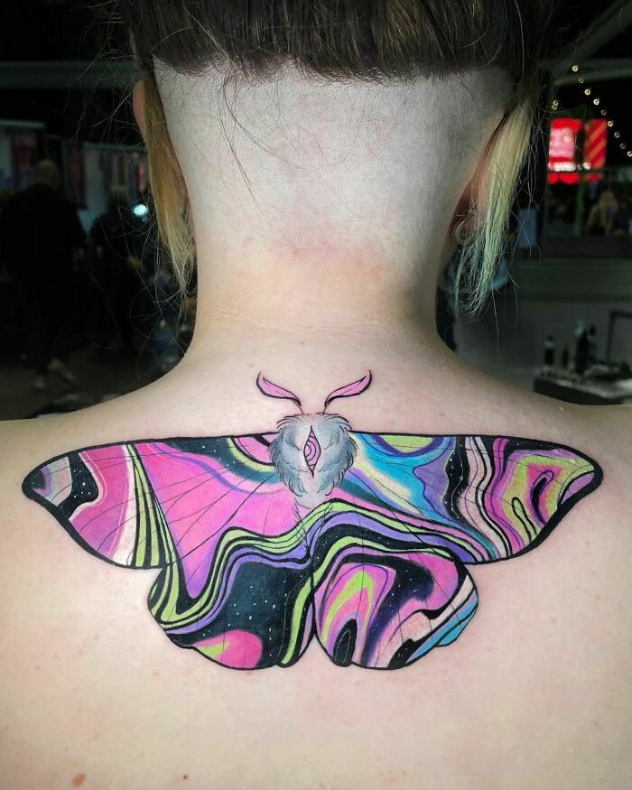 Colorful watercolor tattoo of a moth on the back of a person's neck, featuring ethereal pink and black swirls.