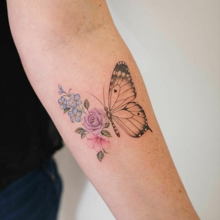 Watercolor tattoo featuring a butterfly with delicate flowers on a person's arm.