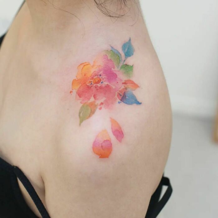 Colorful watercolor tattoo of a flower on shoulder, showcasing ethereal artistic design.