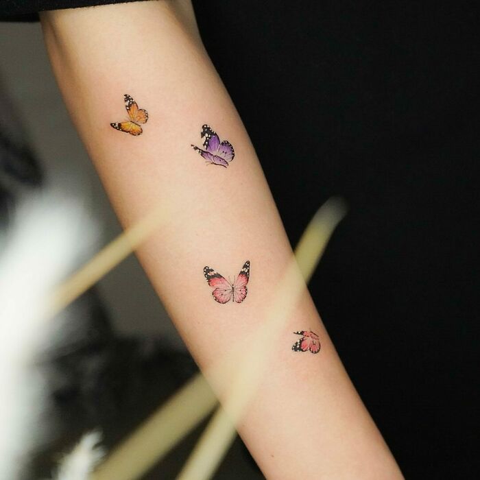 Watercolor butterfly tattoos on forearm, showcasing beautiful ink art.