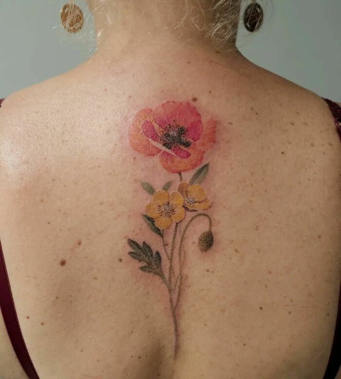 Watercolor tattoo of red and yellow flowers on a person's back.