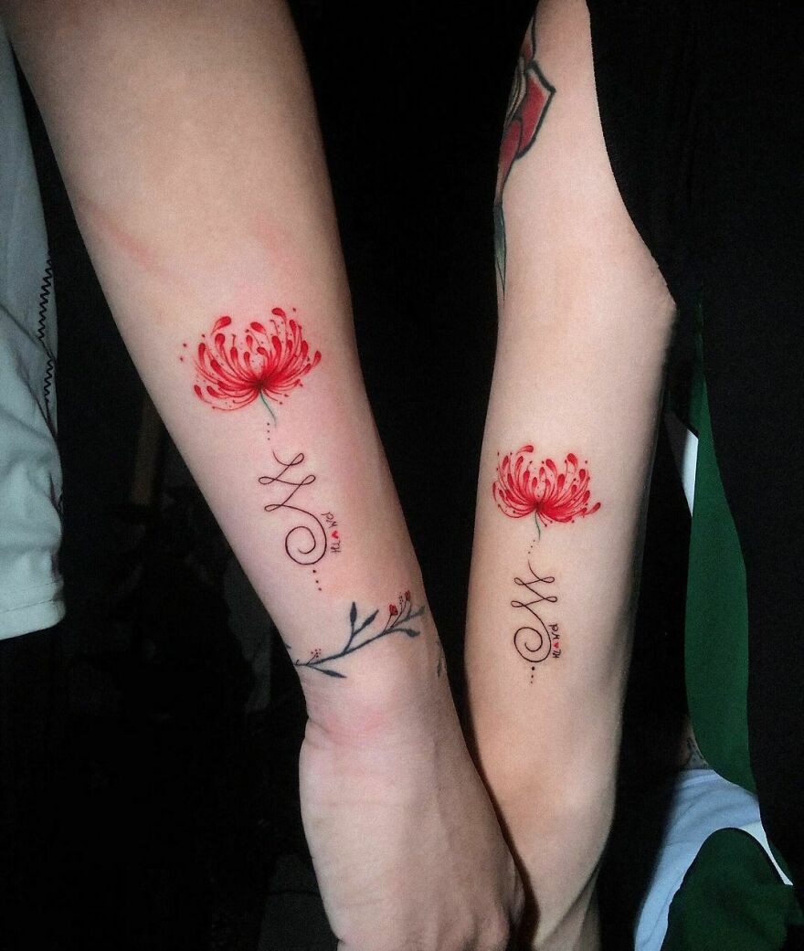 Matching floral watercolor tattoos on two forearms, featuring delicate red flowers and script designs.