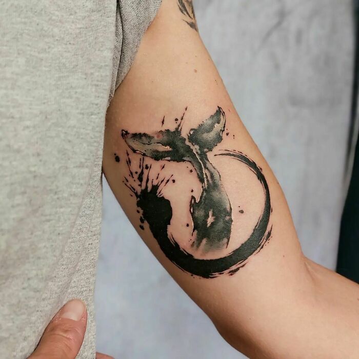 Watercolor tattoo of a whale tail on an arm, showcasing artistic inkspiration.