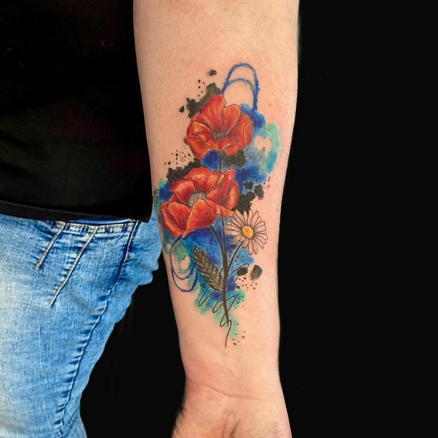 Vibrant watercolor tattoo of red poppies and blue splashes on forearm, showcasing artistic ink designs.