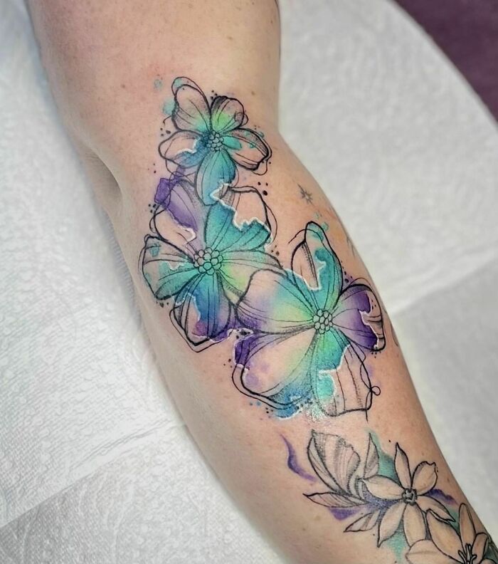 Colorful floral watercolor tattoos on forearm, blending vibrant blues and purples for ink inspiration.
