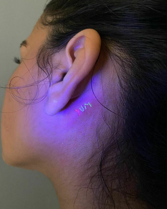 Glow-in-the-dark word tattoo behind the ear showcasing unique ink ideas.