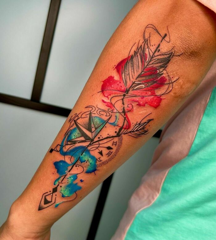 Watercolor tattoo on a forearm featuring vibrant red, blue, and green hues with abstract and geometric designs.