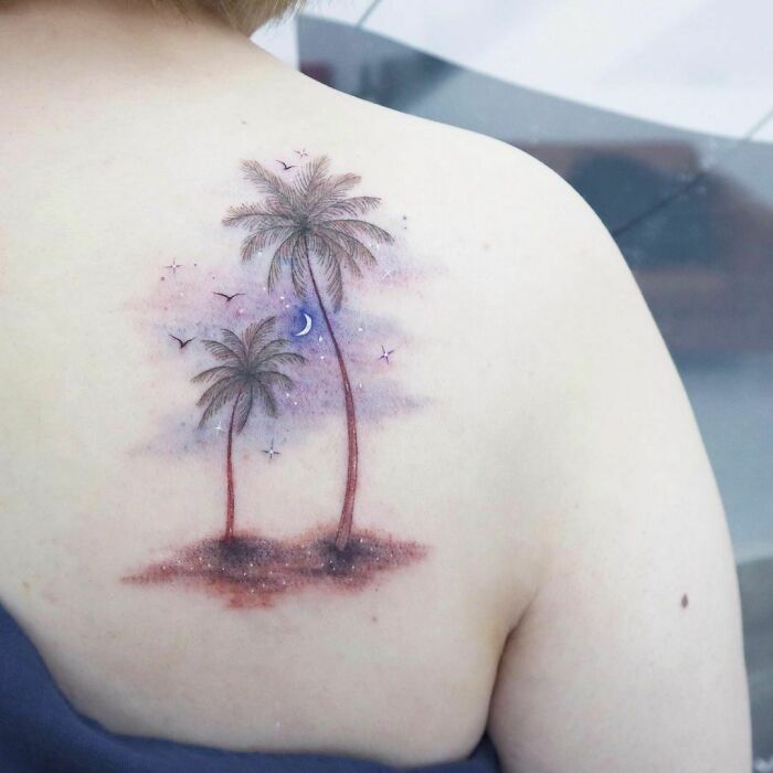 Watercolor tattoo of palm trees on back, featuring a night sky with stars and a crescent moon.
