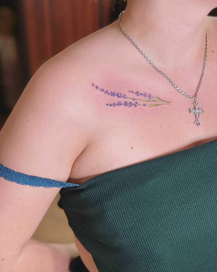 Watercolor tattoo of lavender sprigs on a shoulder, complementing a silver cross necklace.