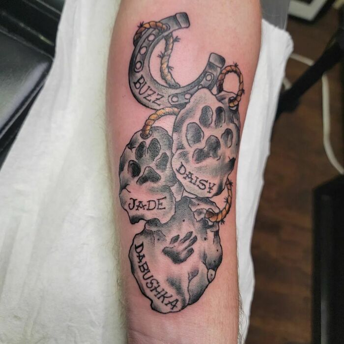 Pet tattoos featuring paw prints and names on an arm, symbolizing human-animal bond.