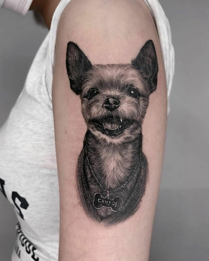 Pet tattoo of a smiling dog on an arm, showcasing detailed fur and a name tag.