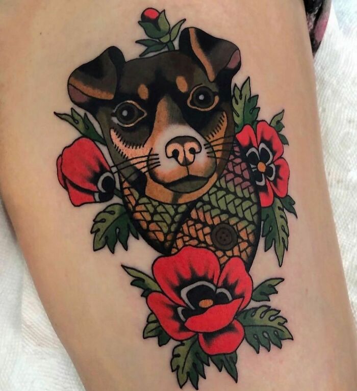 Pet tattoo depicting a dog's face surrounded by vibrant red flowers and green leaves.