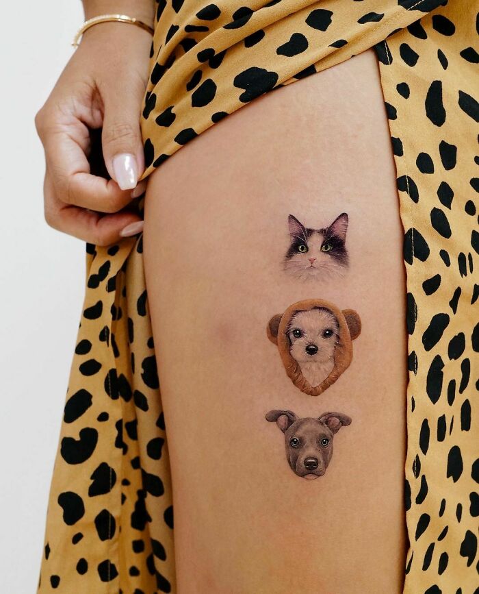 Pet tattoos of cat and two dogs on a person's thigh, featuring realistic art and black-spotted fabric.