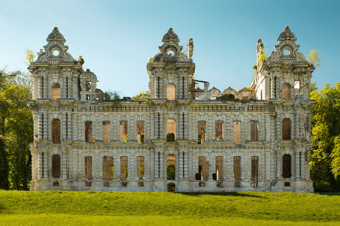 Abandoned castle ruins with empty windows surrounded by greenery under a clear blue sky, showcasing beautiful historic architecture.