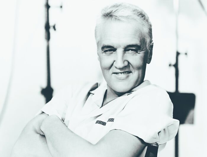 AI-generated image of a celebrity smiling, wearing a patterned shirt, imagined as if they were alive today.