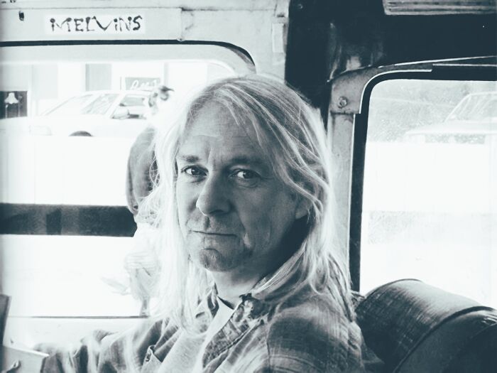 AI-generated image of a celebrity, with long hair, sitting inside a vehicle, looking towards the camera.