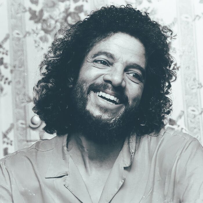 AI-generated image of a smiling man with curly hair and a beard in a vintage shirt.