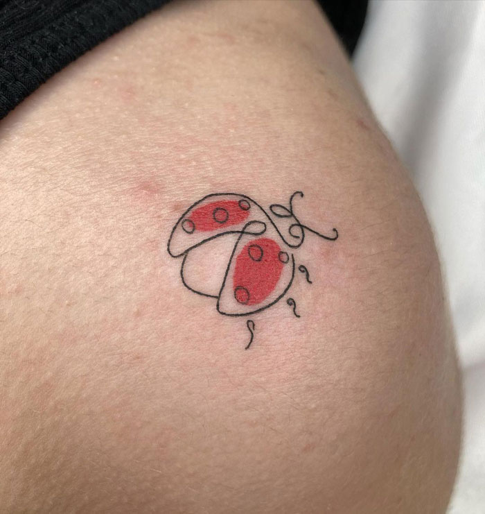 Minimalist animal tattoo of a ladybug with red wings and black dots on skin.