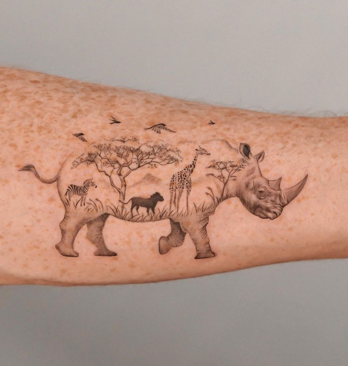 Rhino tattoo featuring various animals and trees on an arm, celebrating the animal kingdom.