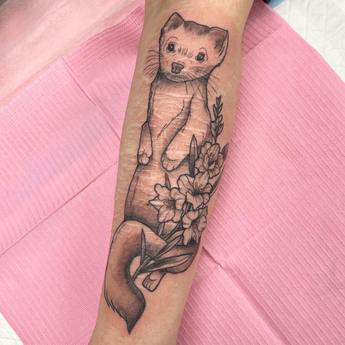 Realistic animal tattoo of a ferret with flowers on forearm, showcasing simplicity and artistry.