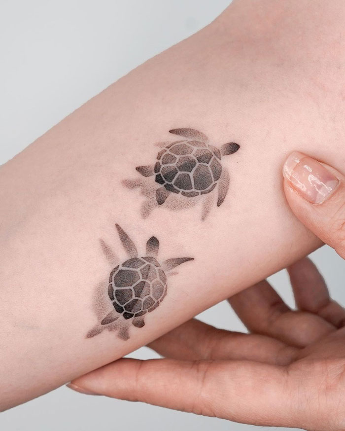 Simple realistic animal tattoo of two small turtles on forearm.