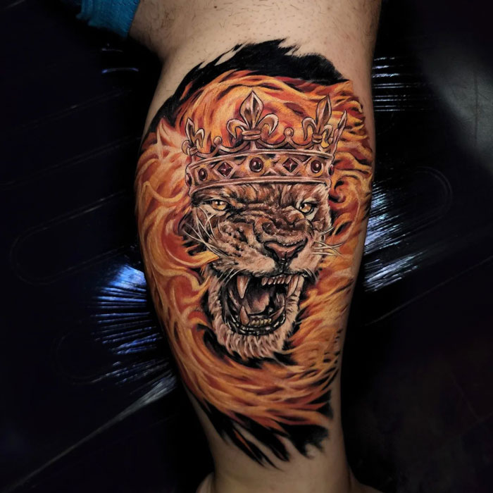 Lion tattoo with crown and fiery mane on leg, showcasing striking animal tattoo details.