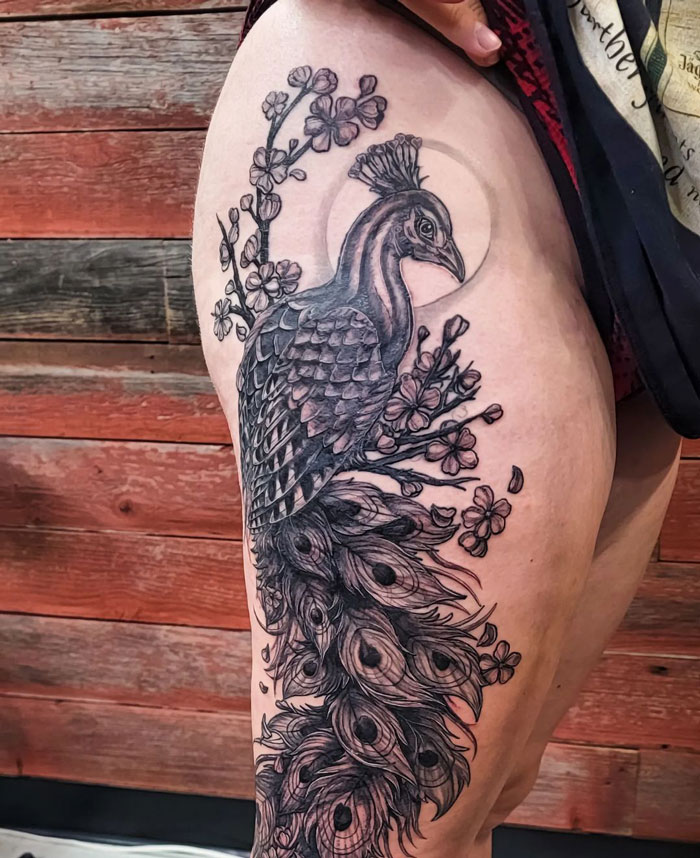 Detailed peacock tattoo on a person's thigh, showcasing the beauty of animal tattoos with intricate feathers and floral elements.