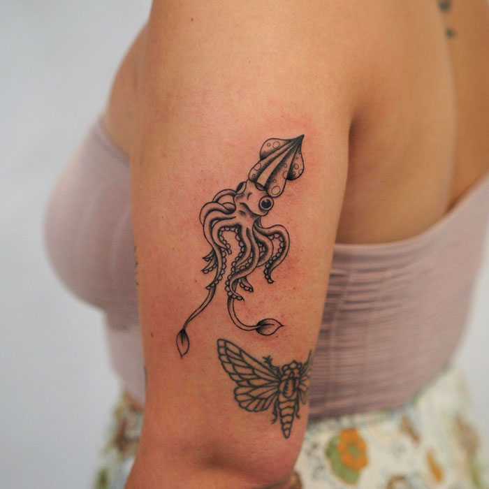 Animal tattoo of a squid inked on a person's upper arm, featuring intricate details next to a moth design.