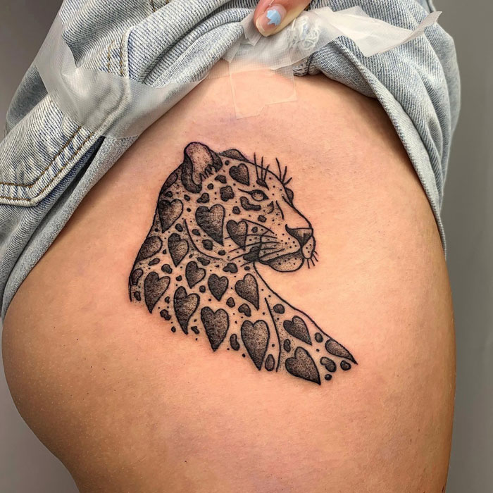 Animal tattoo of a leopard with heart-shaped spots on upper leg.