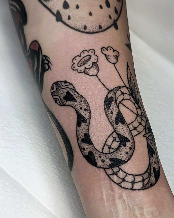 Snake tattoo with floral elements on arm, showcasing intricate animal tattoo art.